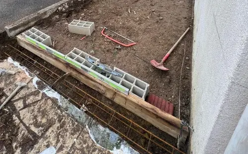 Fouille coffrée et ferraillée au pied d'un mur, avant le coulage des fondations
